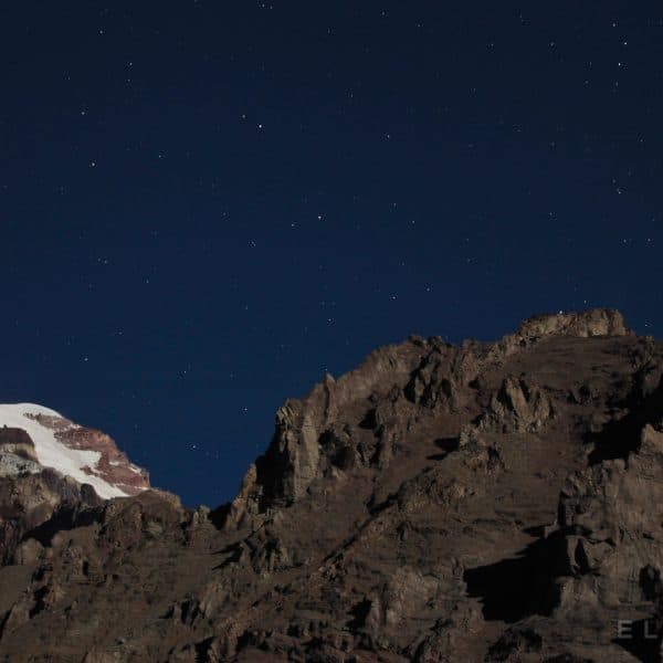 Summit of a rocky and snowy mountain at night with stars