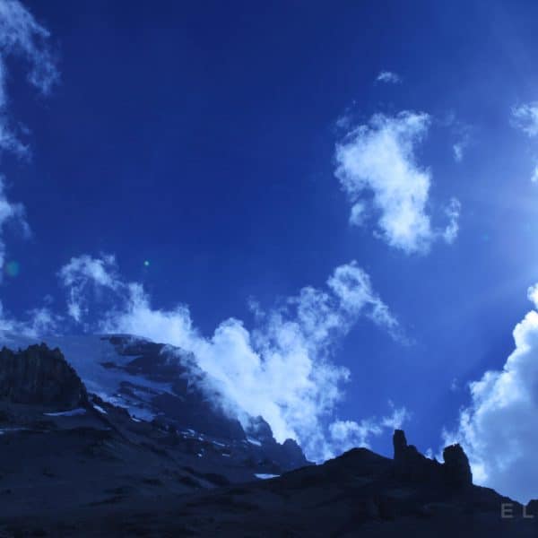 A blue sky with the sun setting over the summit of a mountain with a glacier near the top