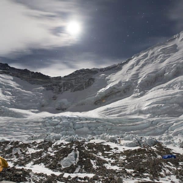 Two yellow tents on a rocky glacier overlook the moon setting in a glaciated area on Mt Everest