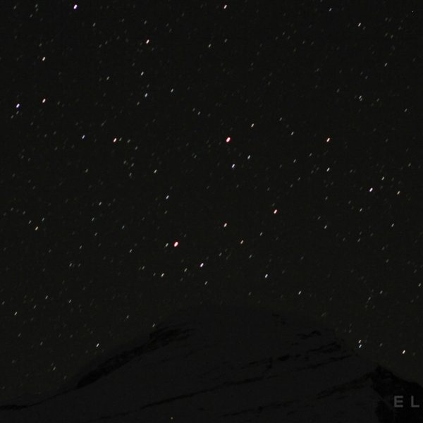 Stars over the summit of a silhouetted summit in Tobet called Cho Oyu with a steep slope icy slope leading to the top
