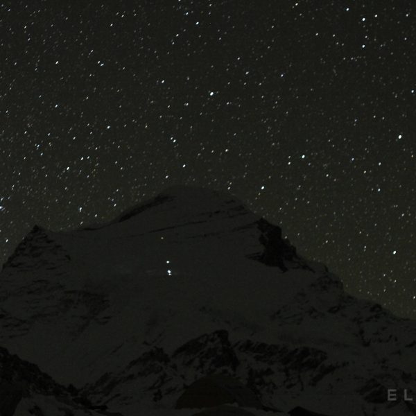 An impressive snow capped mountains with a starry sky at night with climbers headlamps visible half way up the mountain