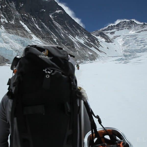 Climbers walk on a glacier with backpacks and ski poles towards Mt Everest and Mt Lhotse