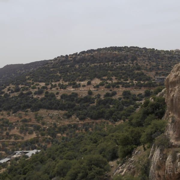 A climber wearing a bluw shirt abseils off a cliff with hills and a few Arabic style homes in the distance
