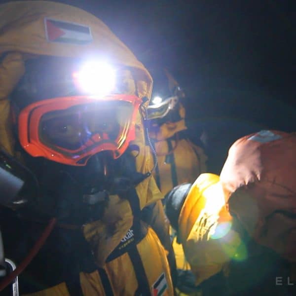 Climber dressed in an orange downsuit wearing a headlamp and heavy climbing equipment and bright orange goggles