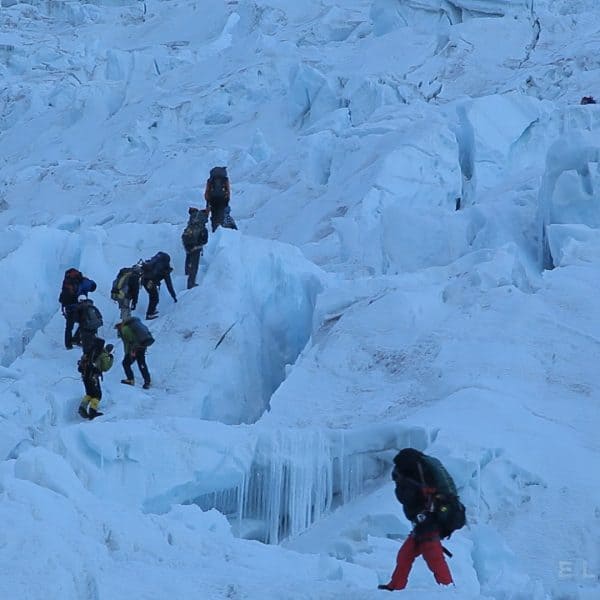 A group of Sherpas walking with backpacks on a glacier called the Khumbu Icefall near Mt Everest with other climbers in the distance