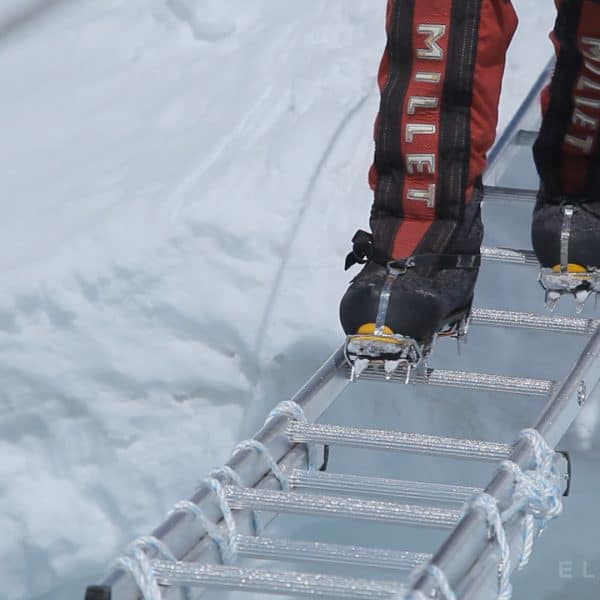 A climbers red boots seen lose up wearing crampons crossing an aluminum ladder suspended over a crevasse on Mt Everest