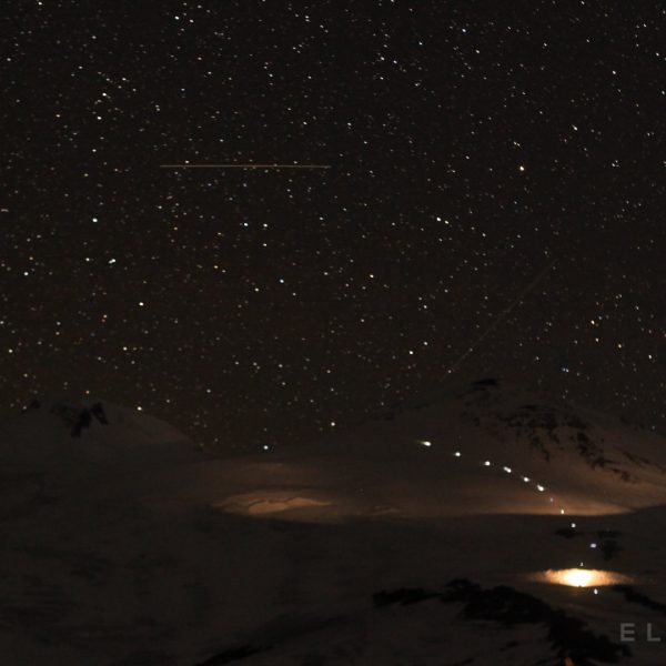 Twin peaks with a shooting star across the sky as climbers with headlamps appear to make their way towards the top