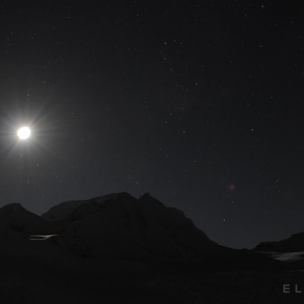 Moon rises high in the starry sky over a snow capped peak in the Himalayas