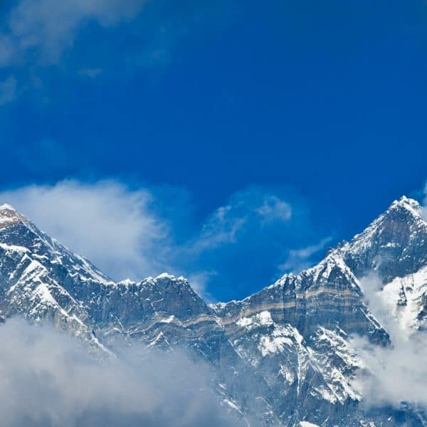 Two high rocky mountain peaks with snow and tellow markings surrounded by clouds and a blue sky