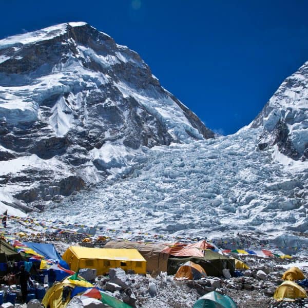 Multi colored tents at the base of a snowy glacier mid day in the Himalyas with mountains in the distance near Mt. Everest