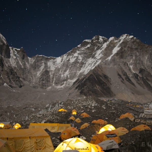 Yellow tents illumated at night with headlamps on a rocky glacier on Mt Everest with stars