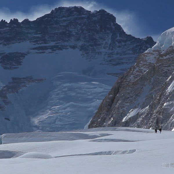 5 climbers walk across a glacier in single file with a tall mountain known as Lhotse in the distance