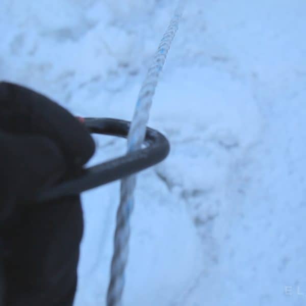 A close up of a hand holding a carabiner following a rope on an icy glacier in the Khumbu Icefall on Mt Everest