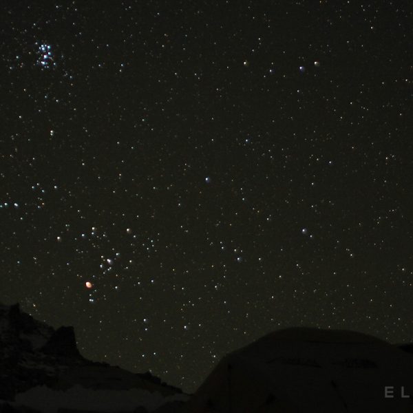 Impressive sky of stars with silhouetted tents in the foreground next to a mountain ridge