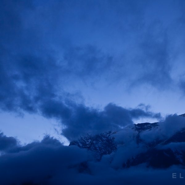 A mountain is surrounded by blueish purpleish clouds in the Himalayas