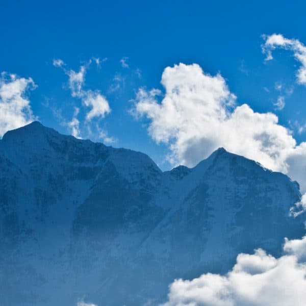 A tall Himalayan snow capped mountain surrounded by clouds and a blue sky
