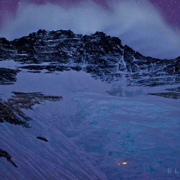 A steep icy face on a mountain called Lhotse at night with a purplish sky as stars move across the sky