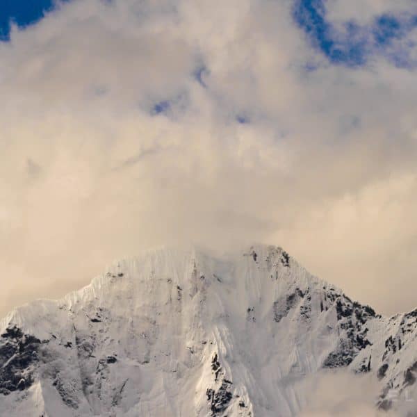 A himalayan snow capped summit with cloud formations at sunset with a blue sky