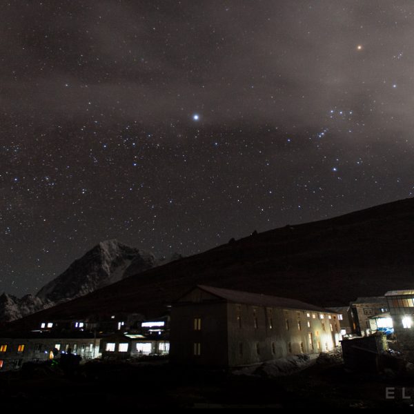 Stone hotels in the mountains in Nepal in a valley with stars in the background at night as the moon sets in the distance