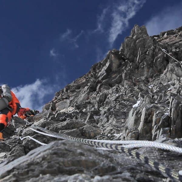 A climber in a red down suit climbs a rocky section on Mt Everest with ropes seen in the foreground