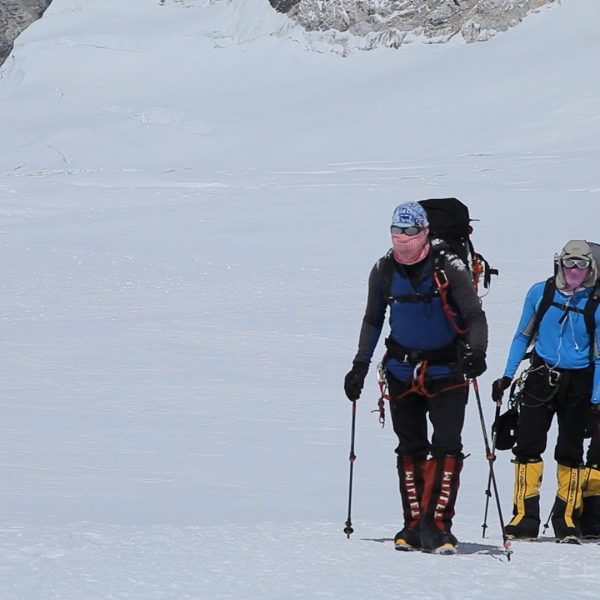 Climbers dressed lightly in multi colored clothing walk on a glacier in single file towards their destination