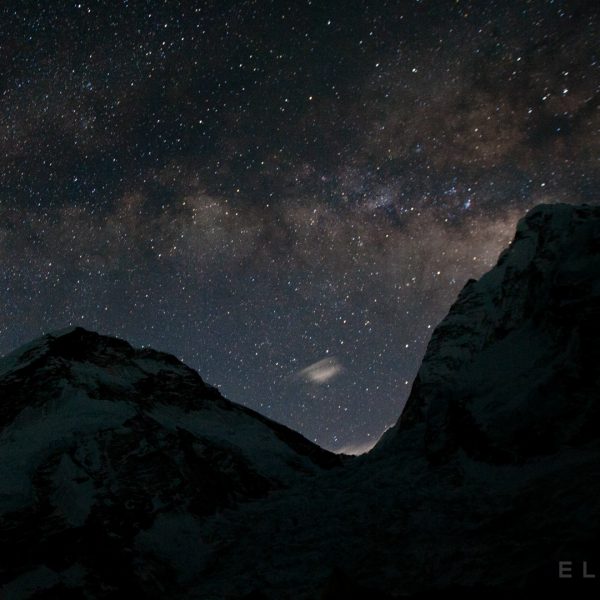The Milky Way rises above two mountains at night with a glacier in between them with stars in the sky