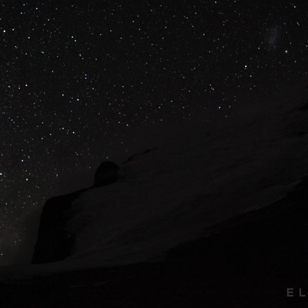 The Milky Way is faintly visible in the night sky with a mountain in the foreground with a snowy trail at night