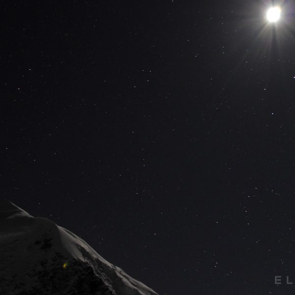 Moon rises high in the starry sky over a snow capped peak in the Himalayas