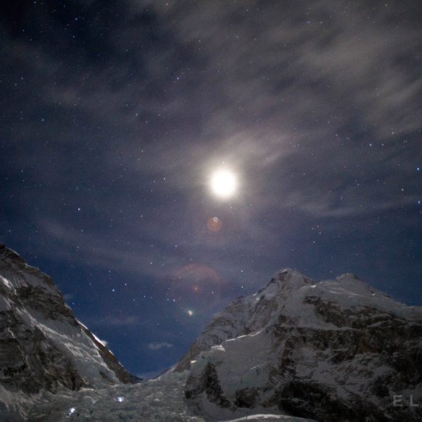 The moon rises at night above two mountains near Mt Everest with stars in the sky as clouds pass