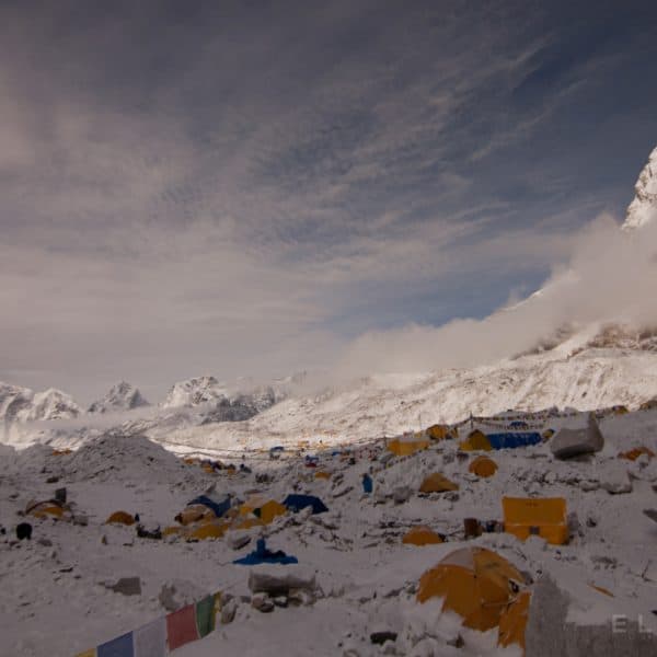 Multi colored tents on a snowy glacier in the Himalyas with mountains in the distance at sunrise