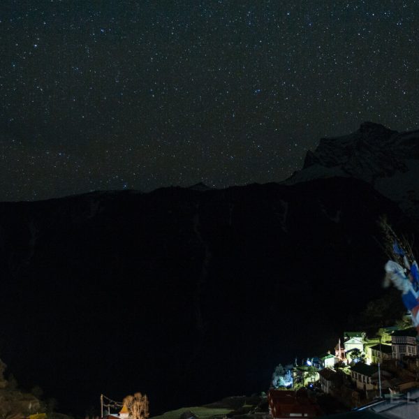 A village with colorful stone hotels carved into the side of a mountain at night with stars in the distance