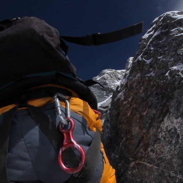 An exhausted climber breathing supplemental oxygen through a mask struggles as he walks over a dangerous rock with high exposure beneath him on Mt Everest