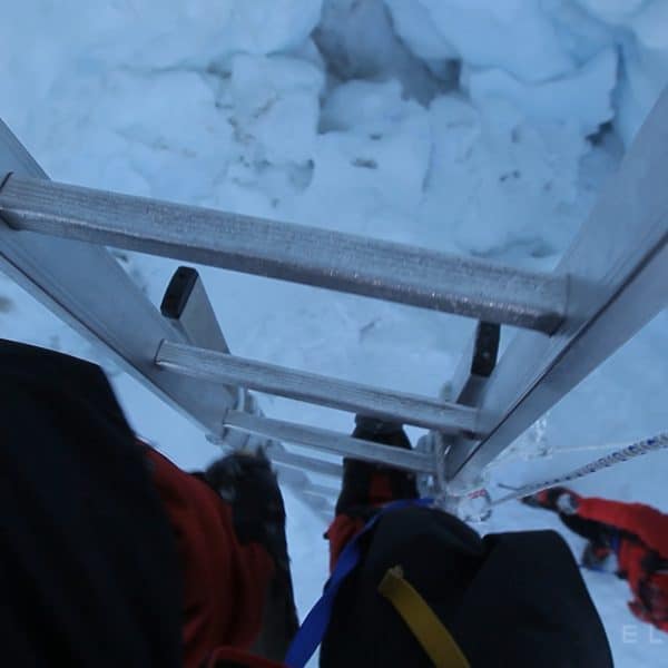 A cameramans perspective climbing an aluminum ladder with one hand in the Khumbu Icefall near Mt Everest