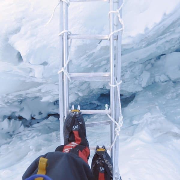 Climbers point of view looking down and crossing a dangerous aluminum ladder with a deep crevasse below on Mt Everest