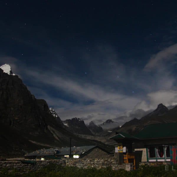 Stone houses and stone walls in a valley at night with mountains and stars in the background