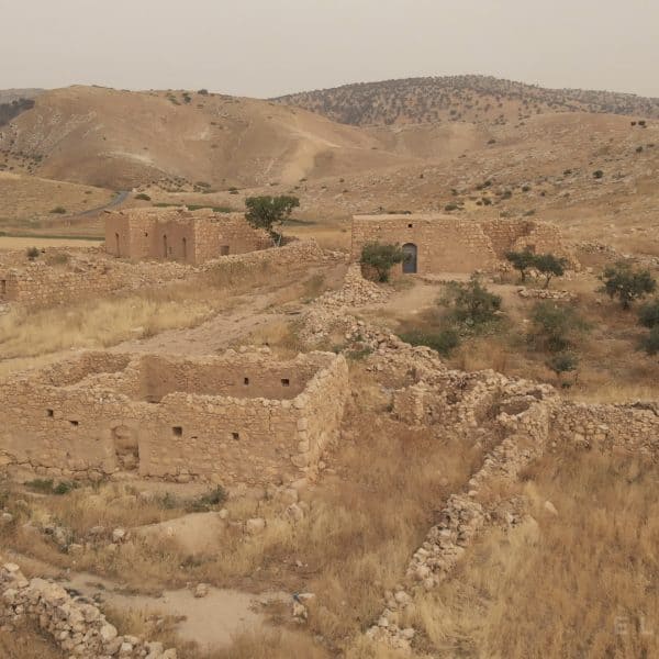 Jordanian brown colored ancient ruins in fields of yellow vegetation with small hills in the distance