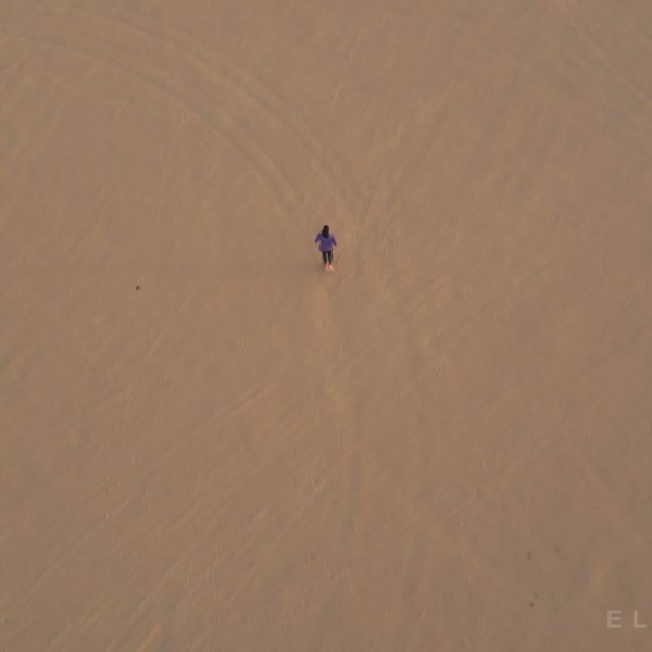 A high angle view of a veiled athlete run in the desert outside of Dubai at sunset on very flat sandy terrain with some trees in the distances