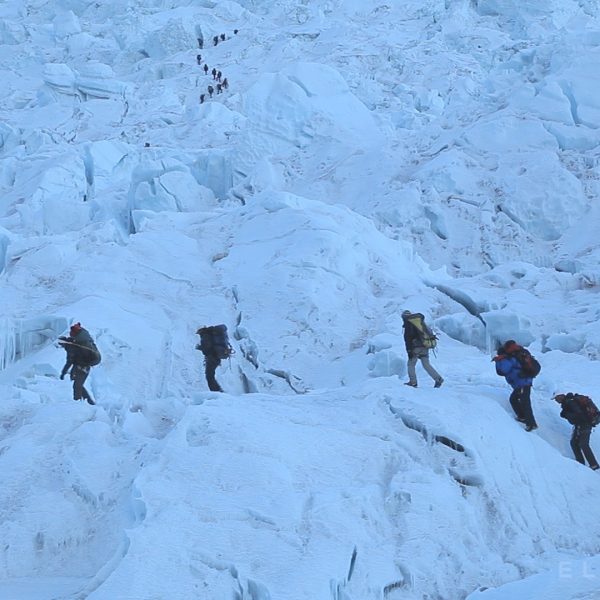 A dozen Sherpas walking with backpacks on a glacier called the Khumbu Icefall near Mt Everest