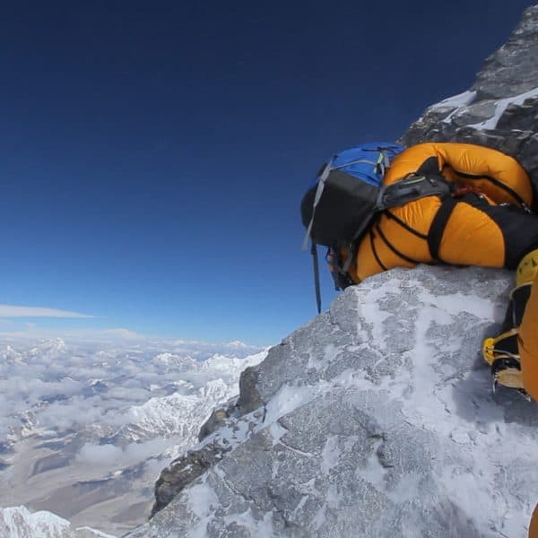 An exhausted climber breathing supplemental oxygen through a mask struggles as he straddles a dangerous rock with high exposure beneath him on Mt Everest