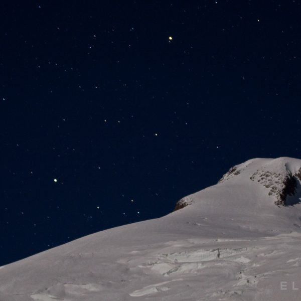 A snowy summit with a starry blueish night sky
