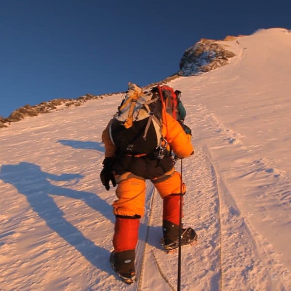 A point of view perspective of a climber at sunsrise on mt Everest holding a blue device called an ascender used to climb a rope