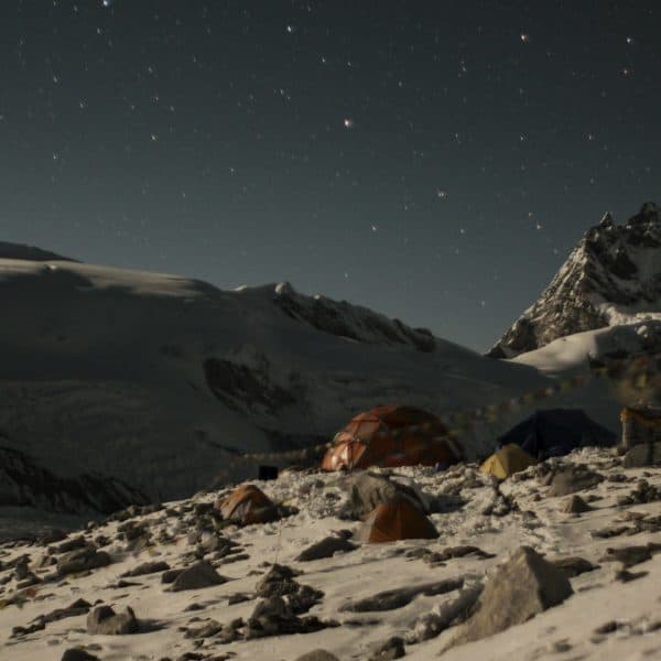 Tents on a snow glacier with a rock altar with prayer flags with stars and snowy mountains in the distance