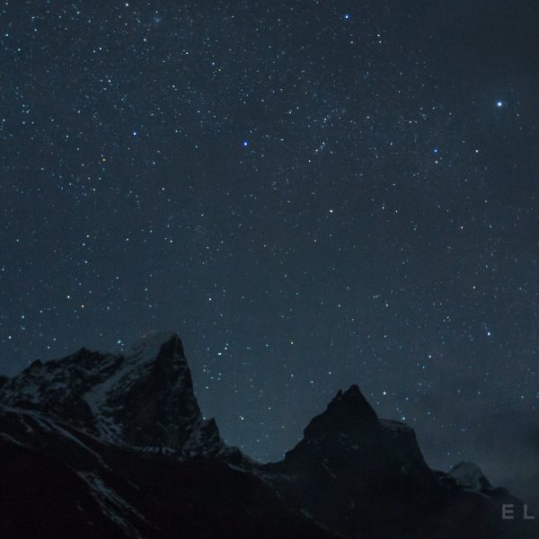 Two triangular shaped peaks stand amongst a starry backdrop with dark cloud formations