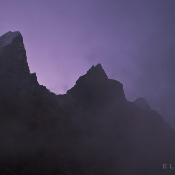 Two steep mountain peaks stand tall amongst a purple sky with dark cloud formations