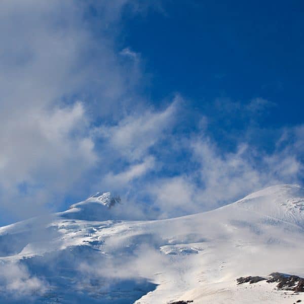 Two twin summit peaks covered in snow with a vibrant blue sky and passing clouds