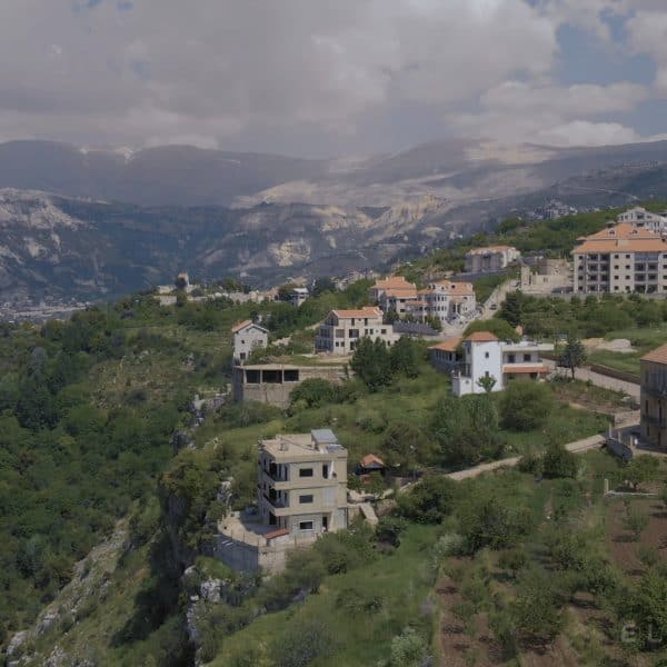Villages in Lebanon with orange roofs perched on the ende of a cliff revealing a valley with mountains and clouds in the distance