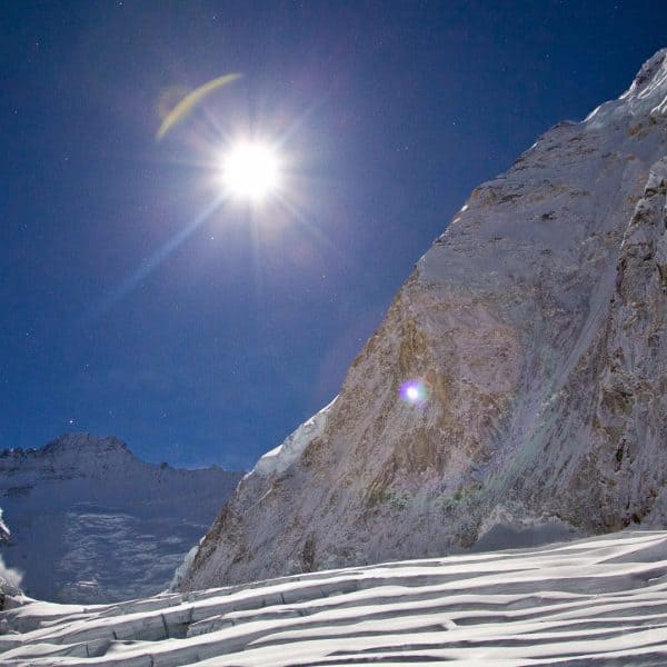 The moon rises at night above a mountain in the distance known as Lhotse and creates a beautiful lens flare with shadows from the light above