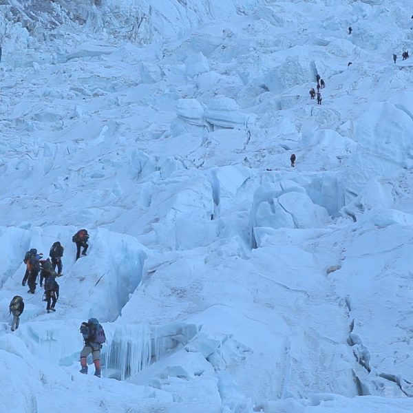 A group of Sherpas walking with backpacks on a glacier called the Khumbu Icefall near Mt Everest with other climbers in the distance