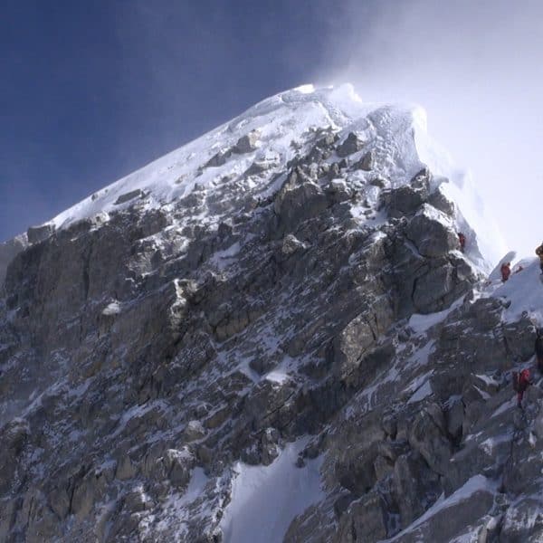 Snow blows off the summit as climbers wearing multi coloured suits on Mt Everest climb a steep narrow rocky ridge on the way to the top of the world