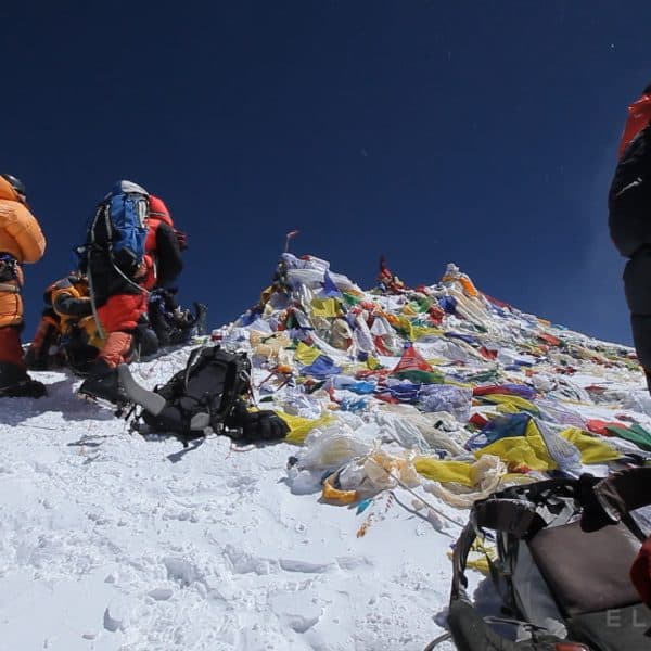 Multi coloured prayer flags mark the summit of Mt Everest as a team of climbers stand with their backpacks on the highest point on Earth